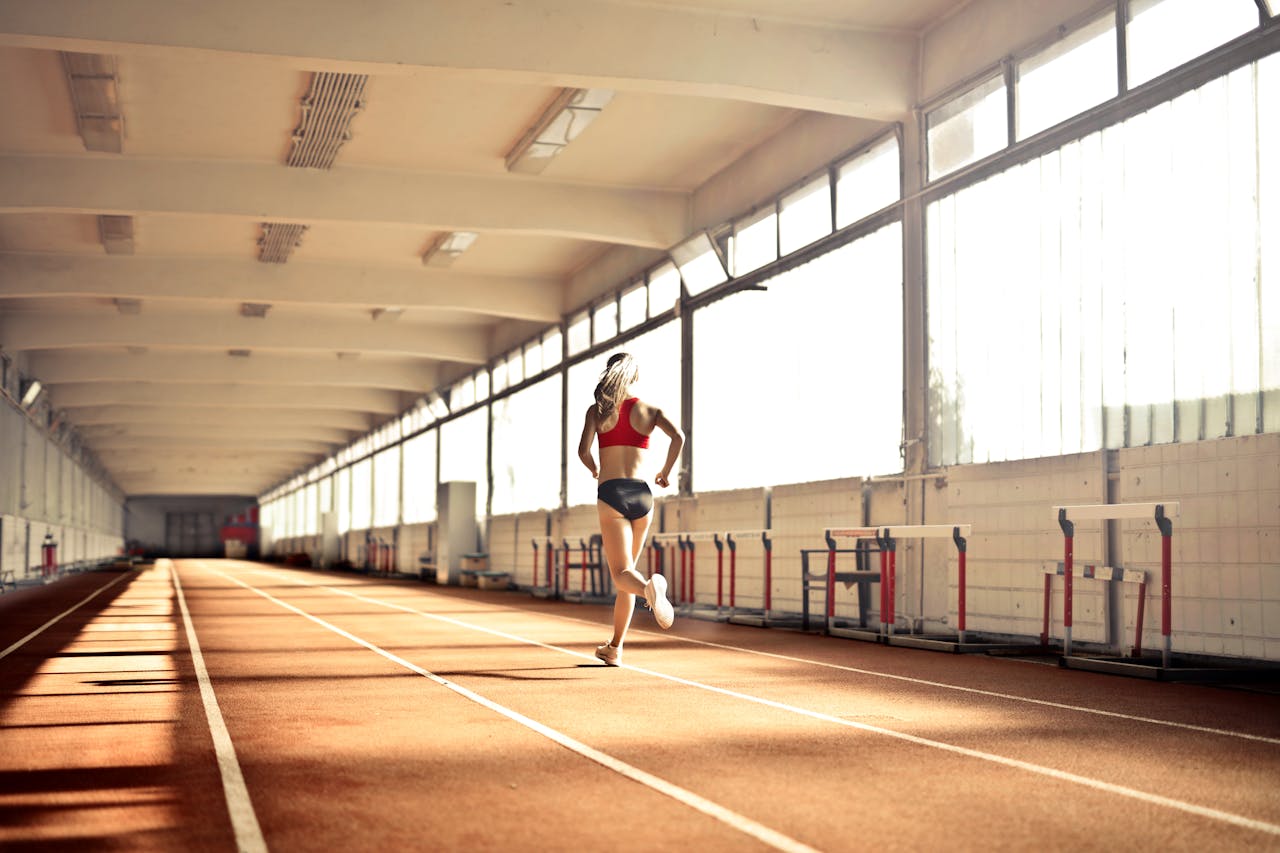 Woman in athletic wear running on an indoor track, showcasing speed and determination.
