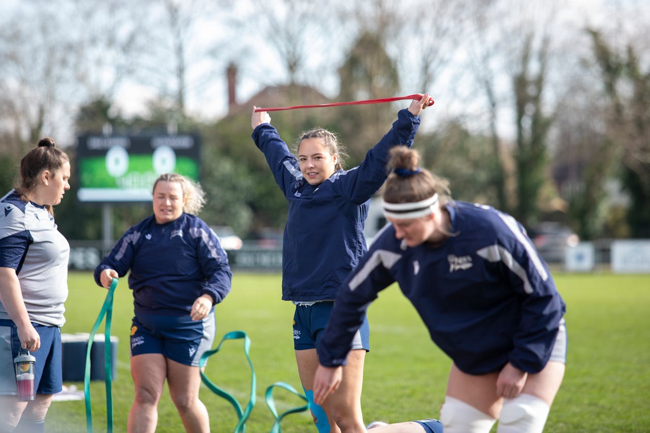 Female rugby team training outdoors with resistance bands on a sunny day.